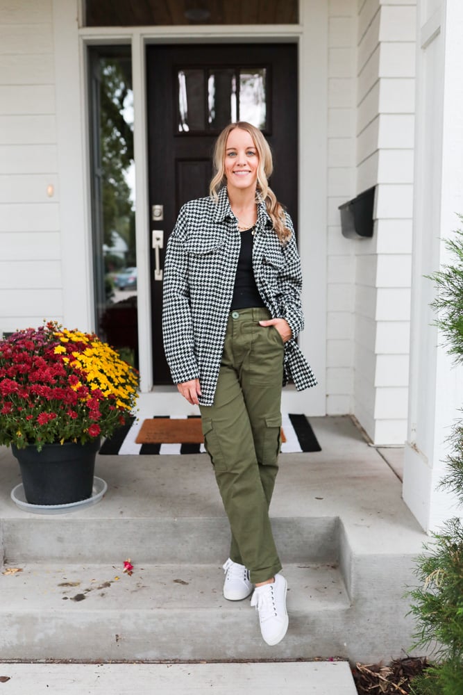 woman wearing green cargo pants, black tank top and herringbone shacket and white sneakers
